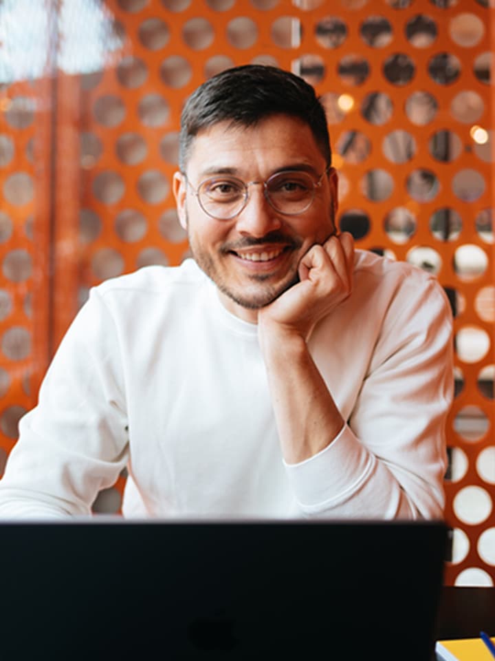 Young man with glasses working on laptop looking at camera