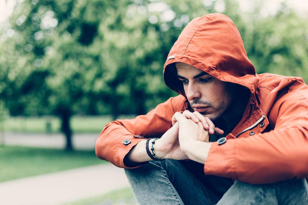 Concerned man in orange hoodie squatting down pensively.