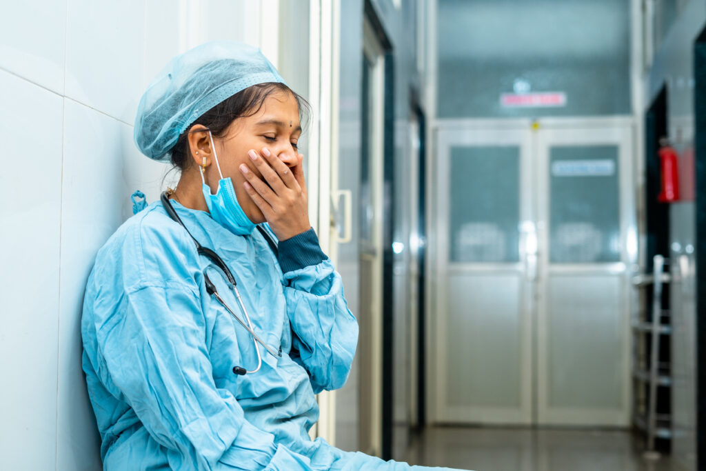 yawning surgeon while sitting at hospital corridor after surgery near operation theatre – concept of exhausted, overworked and boredom