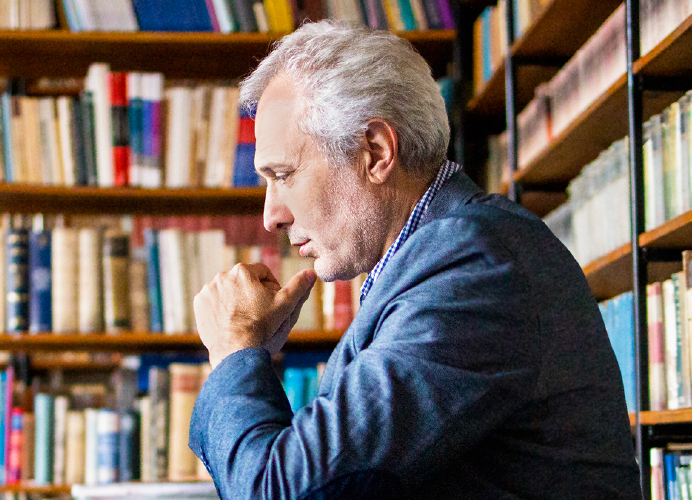 Man pensively contemplating within a library surrounded by books.