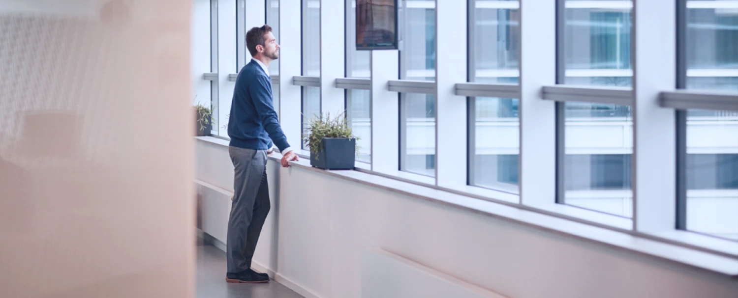 man leaning against window railing looking outside a window at an office