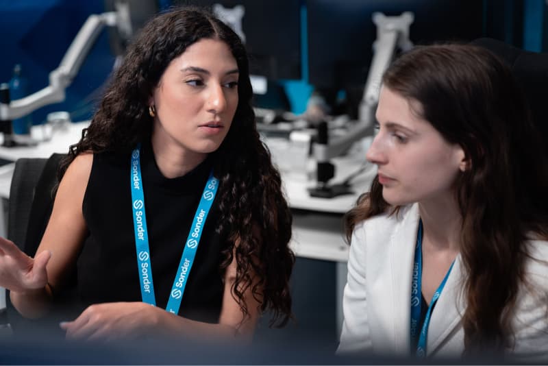 Two Sonder employees engaged in a meeting while seated at their computer desks in an office environment
