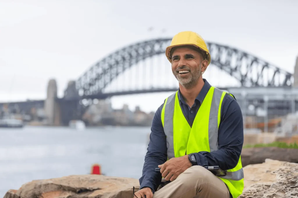 Construction worker smiling posing for a photo with the Sydney Harbour Bridge in the background